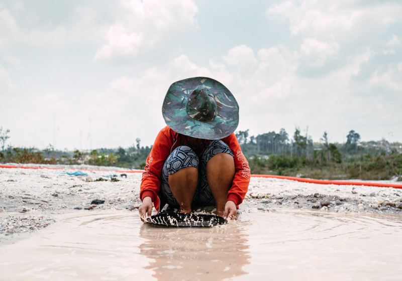 A miner crouched in a river panning gravels for alluvial gold, working without mercury