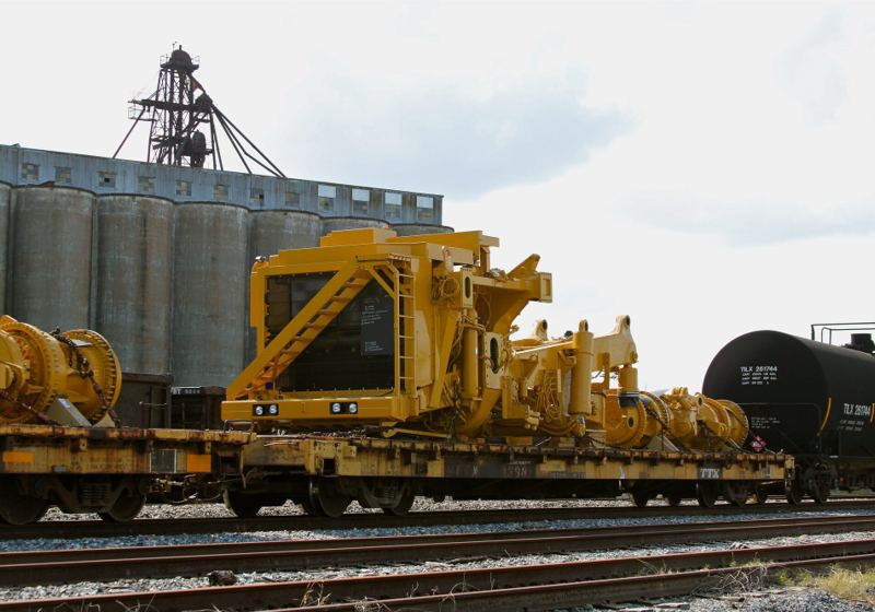 Yellow Caterpillar machine assemblies and final drives chained to rail flatcars